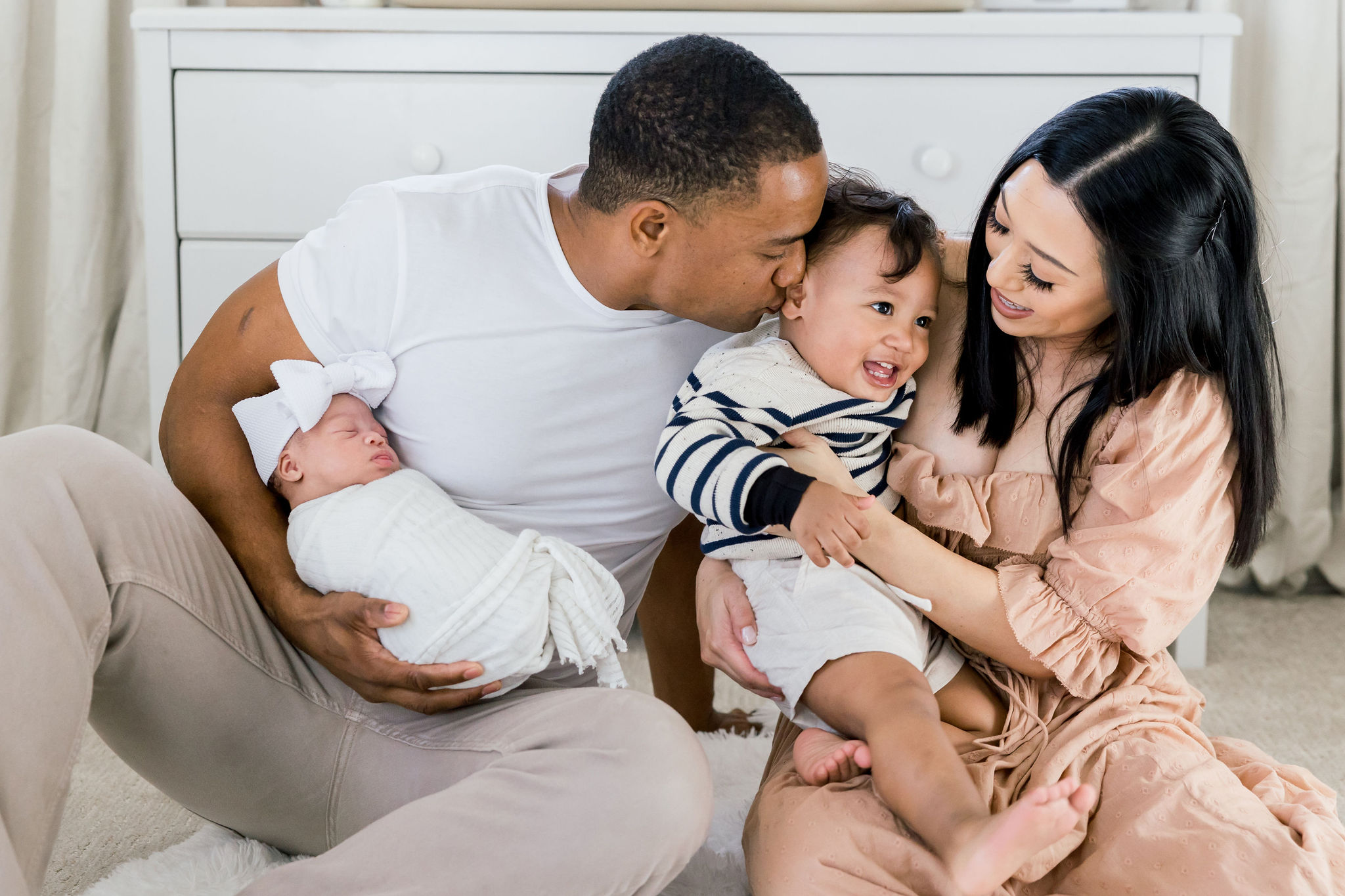 Mom, dad, Roman, and baby Maia snuggling together during her in-home newborn session in Chandler, Arizona. This bright, light, nursery was the perfect setting for her newborn photos.